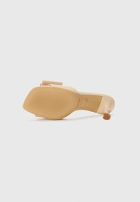Nude hæl sandal med en gennemsigtig strop, gummisål med vandrette riller og en dekorativ sløjfedetalje på fronten.