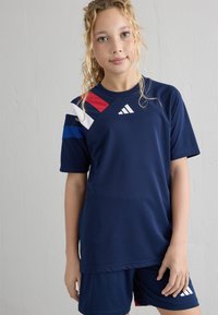 Uniforme atlético azul marino compuesto por una camiseta de manga corta con acentos en blanco, rojo y azul, acompañada de pantalones cortos a juego.