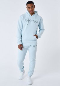 Lichtblauwe katoen hoodie met trekkoorden en een voorzak, gecombineerd met bijpassende joggers. Heeft de opdruk "Project x Paris." Witte sneakers.