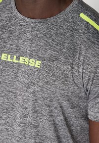 Šedé sportovní tričko s melírovanou texturou, které má výrazné žluté logo "ELLESSE" a neonové akcenty na švech ramen.