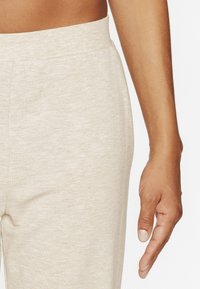 Pantalons de survêtement beige avec une texture douce, dotés d'une taille élastique et d'une coupe ajustée. Main montrée avec une finition naturelle des ongles.