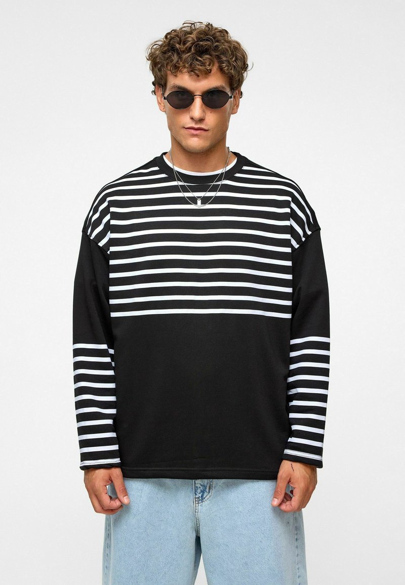 Zwart-witte gestreepte lange mouwen shirt met een losse pasvorm, met horizontale strepen over de borst en mouwen. Draagt met lichtblauwe jeans.