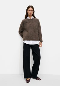 Brown textured knit sweater, long sleeves, wide neckline, layered over a white button-up shirt, paired with black wide-leg trousers and brown studded shoes.