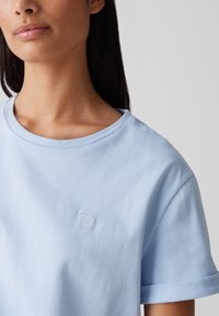 Lichtblauw katoenen t-shirt met een ronde hals, opgerolde korte mouwen en een klein geborduurd hartje op de borst. Gladde textuur.
