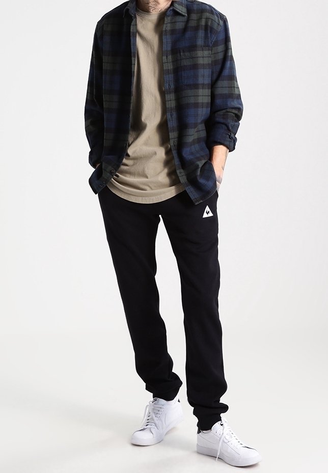 Plaid flannel shirt in dark blue and green, beige t-shirt, black sweatpants with logo, and white sneakers. Casual, layered outfit.