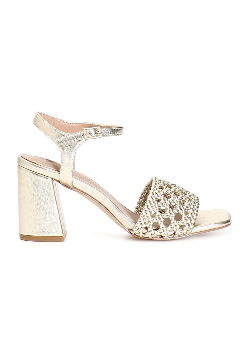 Goldene Sandalen mit Absatz, die ein geflochtenes Oberdesign, eine offene Zehenpartie, einen verstellbaren Knöchelriemen und einen quadratischen Blockabsatz aufweisen. Glatte metallische Oberfläche.