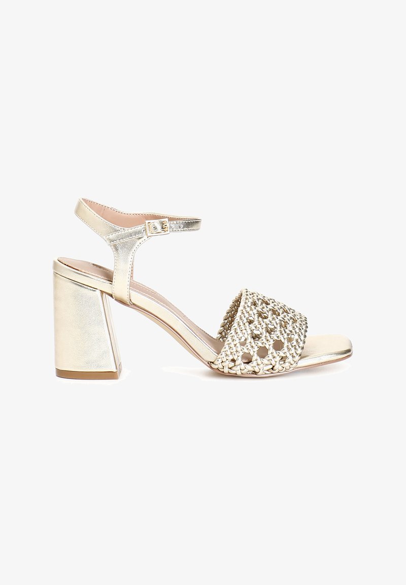 Goldene Sandalen mit Absatz, die ein geflochtenes Oberdesign, eine offene Zehenpartie, einen verstellbaren Knöchelriemen und einen quadratischen Blockabsatz aufweisen. Glatte metallische Oberfläche.