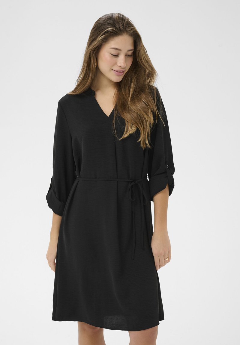 Rochie neagră dintr-un material ușor, cu decolteu în V, mâneci trei sferturi, cordon reglabil în talie și croială lejeră cu tiv ușor evazat.