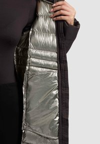 Puffer jacket featuring a reflective silver interior lining, black outer fabric, quilted texture, and a side pocket visible.