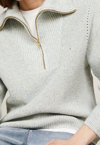 Lysblå halv-zip sweater lavet af struktureret strikstof. Har en hævet krave, subtile stikmønstre og gul lynlåsdetalje.