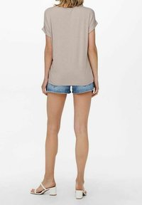 Beige kortærmet top med løs pasform, parret med denimshorts. Hvide block-heel sandaler fuldender det afslappede look.