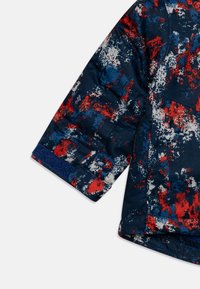 Padded jacket w kolorze granatowym z wielokolorowym, abstrakcyjnym wzorem w odcieniach czerwieni, niebieskiego i białego. Teksturowany materiał z miękkim wykończeniem.