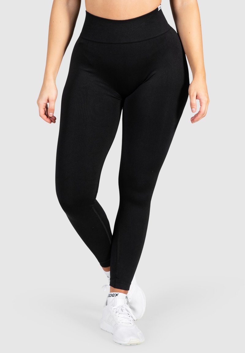 Leggings neri con vita alta, realizzati in morbido tessuto elasticizzato; texture liscia e design aderente. Abbinati a scarpe da ginnastica bianche.