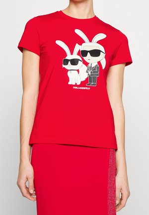 Person wearing a red shirt with cartoon characters—a rabbit and a man in sunglasses—and a matching red skirt with rhinestone trim.