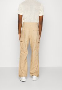 Beiga cargo-byxor med rak bendesign, med sidofickor och en bakre midja. Bärs med en krämfärgad, strukturerad stickad tröja.