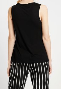 Czarny bezrękawnik z miękkiego materiału, z okrągłym dekoltem. Noszony z czarno-białymi spodniami w paski, prezentującymi pionowe linie.