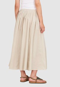 Beige Baumwoll-Maxikleid mit Falten, ausgestattet mit einem breiten Bund und einem Saum, der knapp über den Knöcheln endet. Getragen mit flachen Sandalen.