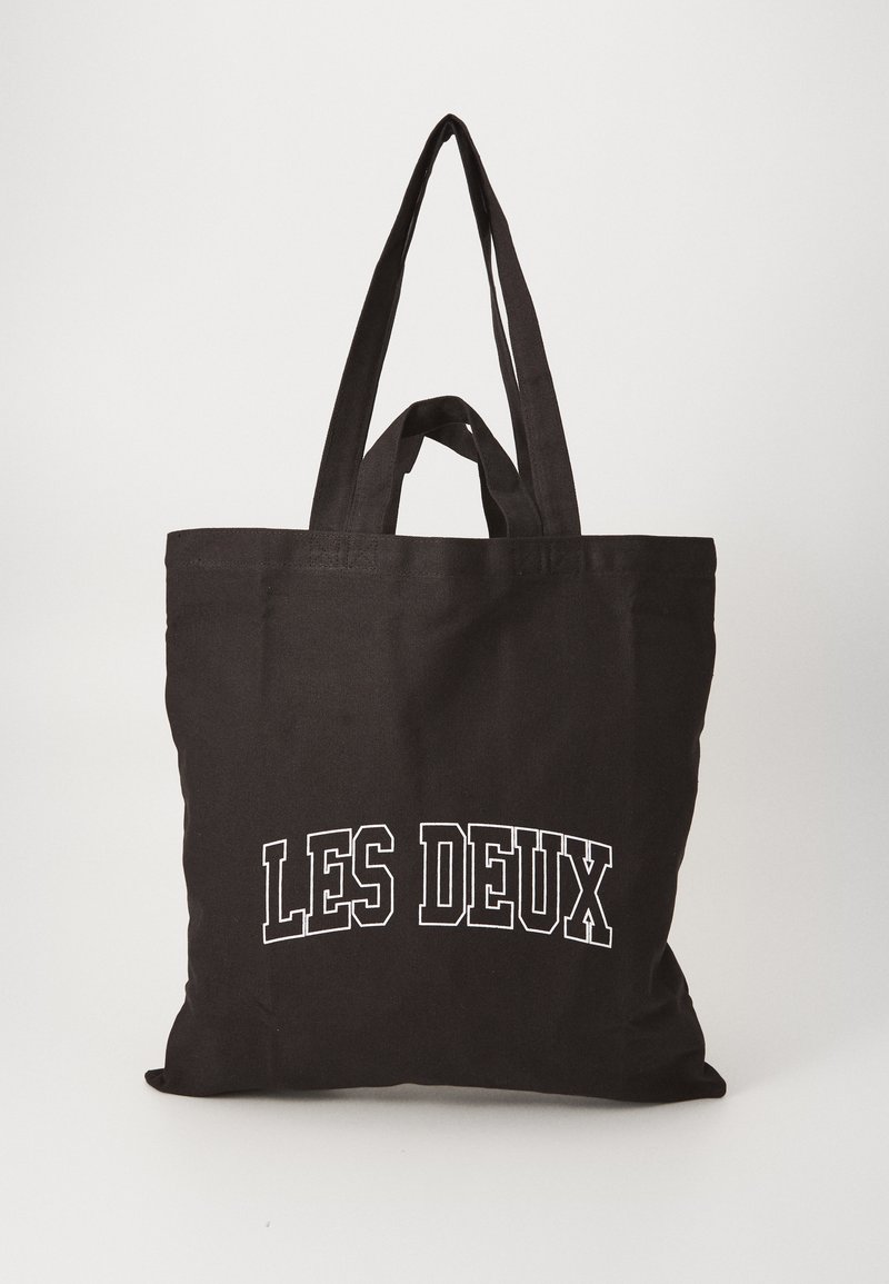 Svart canvas axelväska med två hållbara handtag, pryds av vit text som säger "LES DEUX" på framsidan, slät textur, rektangulär form.