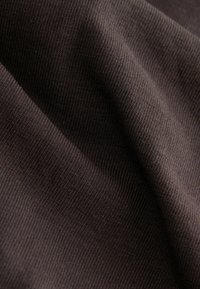 Donkerbruin textiel met een ribbelpatroon, dat een zacht, rekbaar materiaal laat zien dat de weef- en oppervlaktedetails benadrukt.