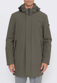 Giacca impermeabile verde oliva con collo alto, cappuccio regolabile e tasche laterali con zip; presenta un design a taglio dritto e cuciture discrete.