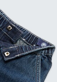 Jeans iz jeansa v temno modri barvi, z vidnimi šivi, kovinsko zapiralo na gumb in strukturo pasu z elastičnimi detajli.
