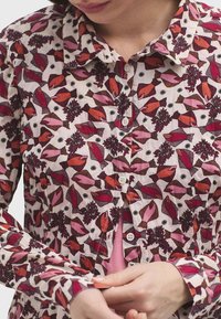 Camisa de algodón con un patrón de peces en rosa y rojo y follaje, con cuello abotonado y puños ajustables, exhibida en un modelo.