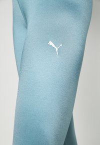Leggings de sport bleu clair fabriqués dans un tissu lisse et extensible. Présentent un logo Puma blanc sur la cuisse. Matériau avec un éclat subtil.