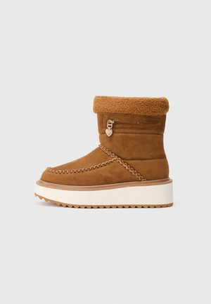 Botas de tobillo de ante color marrón con un puño de borreguillo, costuras decorativas y una cremallera lateral con un charm en forma de corazón. Suela de plataforma con un relieve estriado.