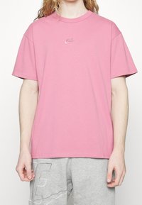 Rosa bomullströja med rund hals, korta ärmar och liten broderad Nike-logotyp på bröstet. Slät textur, avslappnad passform.