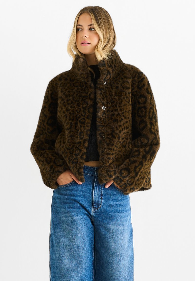 Giacca in pelliccia sintetica a stampa leopardata marrone con colletto alto e chiusura a bottone, abbinata a jeans a gamba larga blu e a un top nero.
