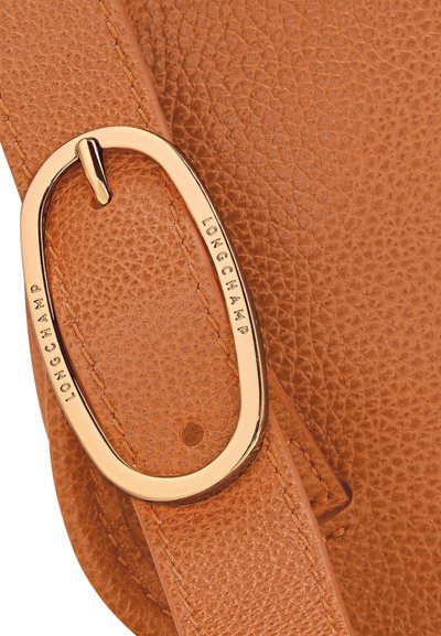 Brauner Leder-Trageriemen mit strukturierter Oberfläche und einer goldfarbenen Metallschnalle, auf der "LONGCHAMP" eingraviert ist.