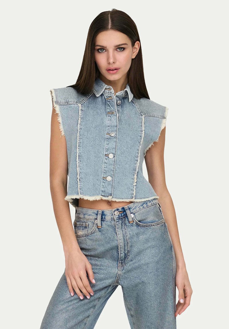 Gilet in denim tagliato, azzurro chiaro, con bordi sfrangiati e chiusura con bottoni. Abbinato a jeans in denim a vita alta. Texture liscia, design senza maniche.