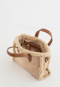 Bolso beige con un borde suave y peludo, detalles de cuero marrón, dos asas y un bolsillo interior con cremallera para mejor organización.