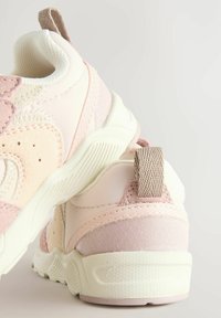 Lyserøde og cremefarvede sneakers med mesh- og ruskindsmaterialer, en formet sål og et løbende hælgreb for nem påtagning.