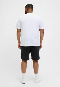T-shirt en coton blanc vue de derrière, associée à un short noir et des baskets blanches, avec des manches courtes et une coupe décontractée.