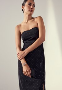 Black strapless dress with white polka dots, a fitted silhouette, side slit, paired with a silver twisted bracelet and clutch.