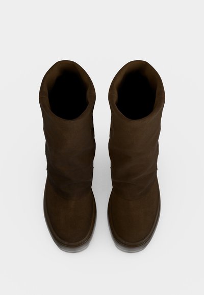 Paire de bottines en daim marron foncé avec des bouts ronds, vue de dessus sur un fond clair uni.