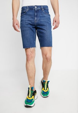 Donkerblauwe denim shorts met een rafelzoom. Gepaard met meerkleurige sportschoenen met mesh- en rubberaccenten.