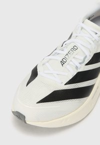 Lightweight white running shoe with black stripes, mesh upper, and textured sole. Features prominent "ADIZERO" branding and flat laces.