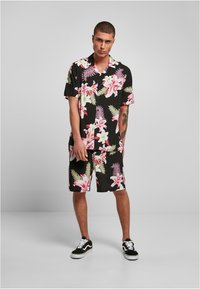 Set de cămașă scurtă cu motive florale și pantaloni scurți, având un fundal negru cu flori roz și albe și frunze verzi. Material din bumbac, croială lejeră.