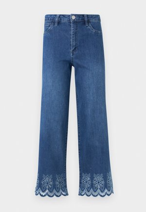 Jean en denim bleu avec une taille haute et des découpes en dentelle florale festonnée le long des ourlets larges des jambes.