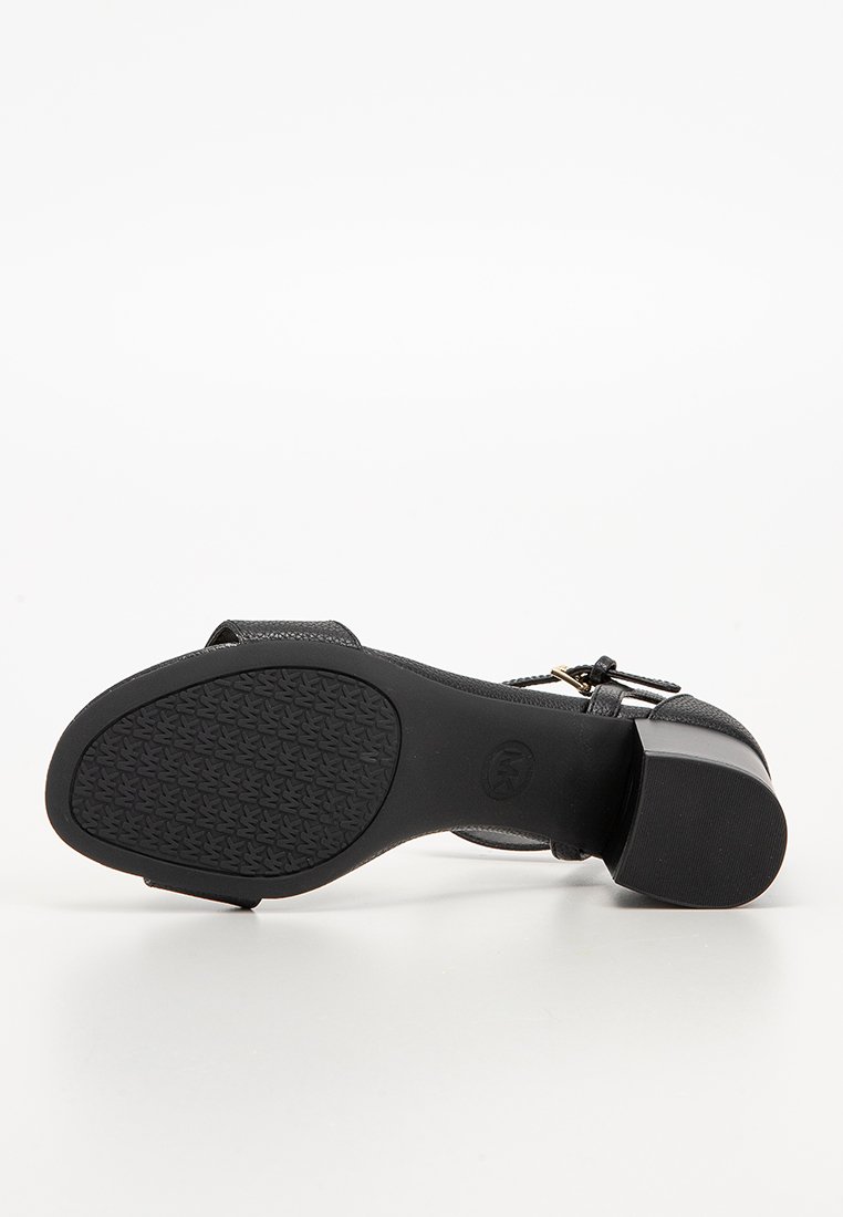 Sandale noire à talons avec une surface texturée, un bout arrondi, une bride à la cheville et une semelle en caoutchouc à motifs. Accent subtil de quincaillerie dorée.