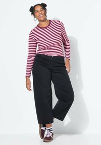 Camisa de manga larga a rayas en burdeos y crema, combinada con pantalones negros de pierna ancha y cintura alta, y zapatillas con detalles en blanco y negro.