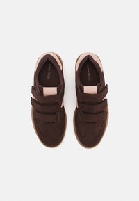 Braune Wildledersneaker mit pinken Akzenten, ausgestattet mit einer strukturierten Oberseite und drei Klettverschlussriemen für den Verschluss sowie einer Gummisohle.