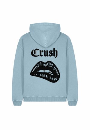Un sweat à capuche bleu clair avec un cordon de serrage, présentant un design de bouche graphique noire et le mot "Crush" au-dessus en texte gras.