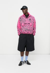 Windbreaker in pink and gray animal print with black Nike Air branding, paired with black shorts, blue socks, and black sneakers.