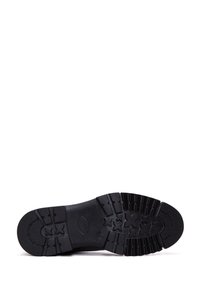 Suela de zapato de goma negra con texturas y surcos, que presenta una puntera redondeada y elementos de diseño elevados para tracción y estabilidad.