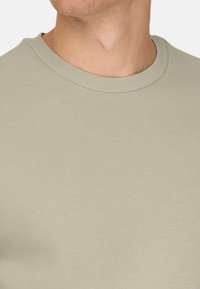 Felpa beige chiaro a girocollo realizzata in morbido tessuto texturizzato. Presenta un collo a costine e una vestibilità classica.