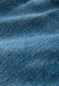 Blauer Denim-Stoff mit glatter Textur, sichtbarem Webmuster und leichtem Glanz über der gewellten Oberfläche.