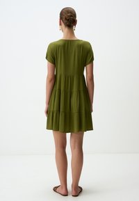 Grünes gestuftes Kleid mit kurzen Ärmeln und rundem Ausschnitt. Aus leichtem Stoff hergestellt, mit lockerer Passform und fließendem Saum.